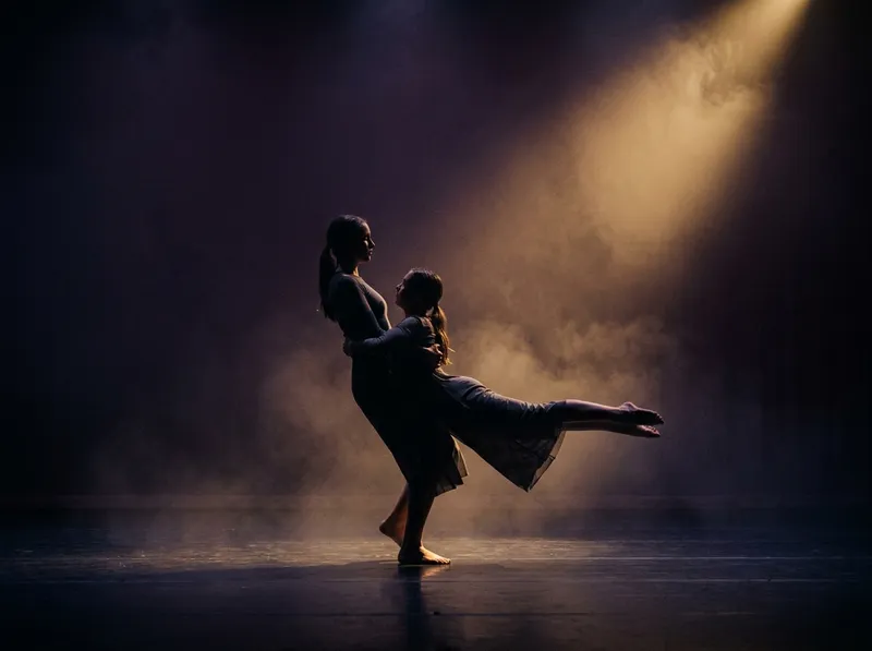 Duas bailarinas adolescentes num dueto de contemporâneo num palco escuro